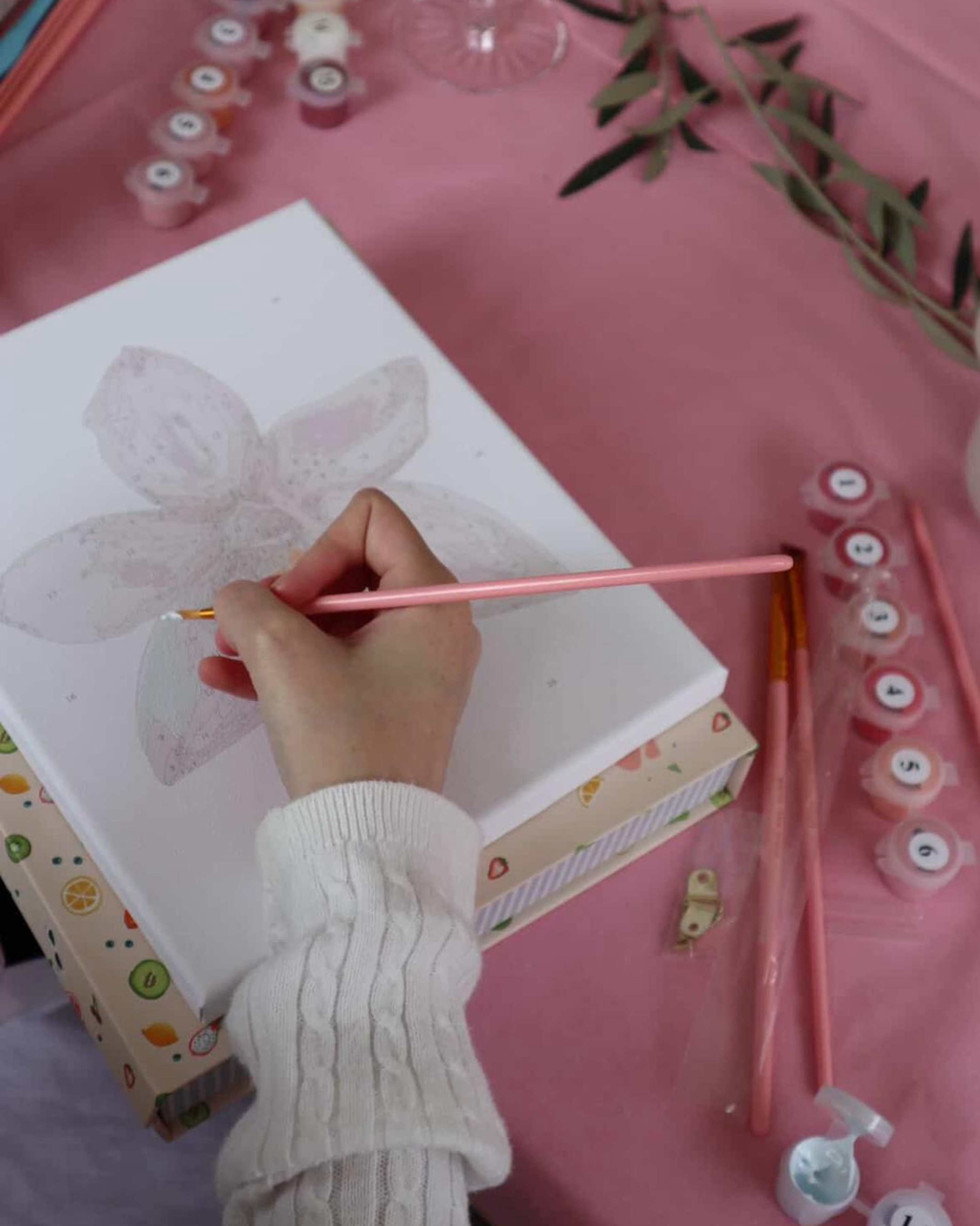 Beginner-friendly orchid paint-by-numbers kit in progress, with soft pink paints, brushes, and creative setup for a fun painting experience.
